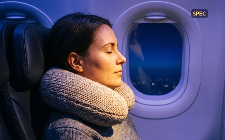 Stand-in photo: a traveler asleep upright in a window seat at night, wearing a travel neck pillow
